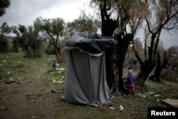 A girl walks next to a self-made shower at a makeshift camp for refugees and migrants next to the Moria camp on the island of Lesbos, Greece, Nov. 30, 2017.