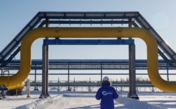 FILE - An employee in branded jacket walks past a part of Gazprom's Power Of Siberia gas pipeline at the Atamanskaya compressor station outside the far eastern town of Svobodny, in Amur region, Russia, Nov. 29, 2019.