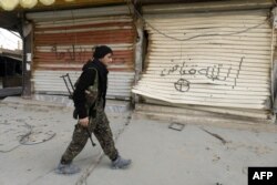 A fighter from the Syrian Democratic Forces (SDF) walks past shops with their fronts painted with the Arabic phrases "beware a sniper" and "caliphate state", in the city of Hajin in Syria's eastern Deir Ezzor province, Jan. 27, 2019.