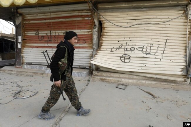 A fighter from the Syrian Democratic Forces (SDF) walks past shops with their fronts painted with the Arabic phrases "beware a sniper" and "caliphate state", in the city of Hajin in Syria's eastern Deir Ezzor province, Jan. 27, 2019.