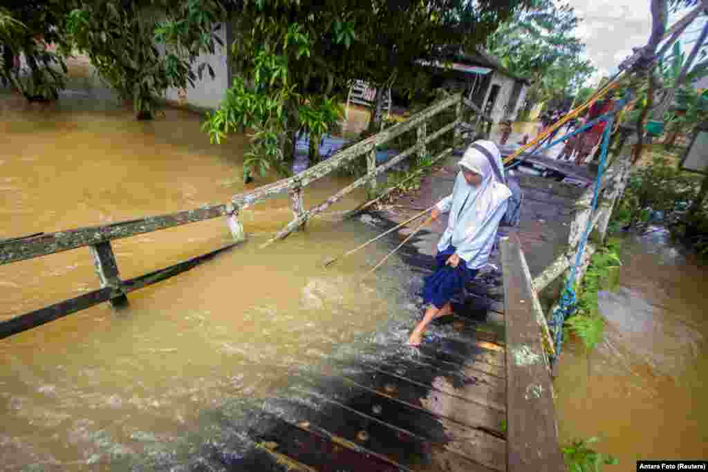 Seorang siswi berjalan melewati jembatan yang rusak akibat luapan sungai menyusul banjir di desa Jaranih, Hulu Sungai Tengah, provinsi Kalimantan Selatan (17/11). (Foto:&nbsp;Bayu Pratama S/Antara via Reuters)