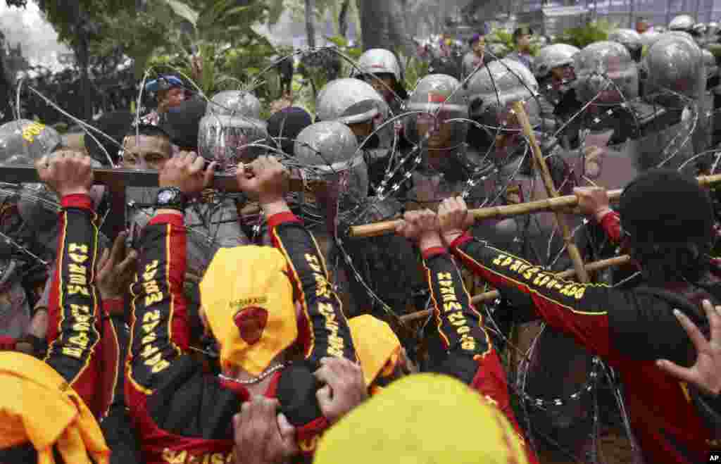 Workers try to remove razor wire which prevents them from marching towards the presidential palace as riot police take defensive position during a May Day rally in Jakarta, Indonesia, Monday, May 1, 2017