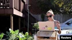 FILE - Kelley Miller, working from home because of the coronavirus disease (COVID-19) pandemic, sunbathes as she works at a standing desk she fashioned from a gardening table on Capitol Hill in Washington, U.S. October 15, 2020. (REUTERS/Jonathan Ernst)