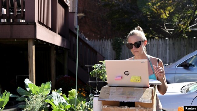FILE - Kelley Miller, working from home because of the coronavirus disease (COVID-19) pandemic, sunbathes as she works at a standing desk she fashioned from a gardening table on Capitol Hill in Washington, U.S. October 15, 2020. (REUTERS/Jonathan Ernst)