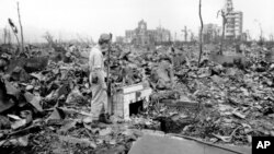 FILE - In this Sept. 7, 1945, photo, an unidentified man stands next to a tiled fireplace where a house once stood in Hiroshima, Japan. 