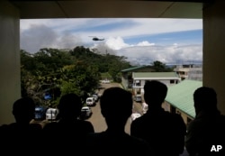 Nasir Abdul (second from right) and other evacuees watch as a military helicopter passes by black smoke from burning houses outside a temporary evacuation center at the provincial government capitol in Marawi city, southern Philippines, June 9, 2017.