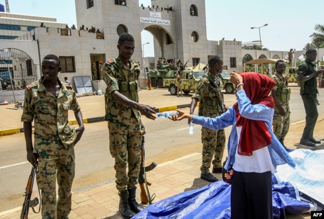 A Sudanese woman hands a bottle of water to a soldier during a rally demanding a civilian body leads the transition to democracy, outside the army headquarters in the Sudanese capital Khartoum, April 12, 2019.