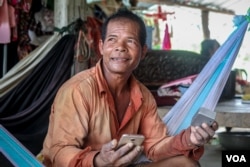 Sum Pha holds his smartphone and a portable speaker which he uses to listen to the news broadcasts. (Khan Sokummono/VOA Khmer)