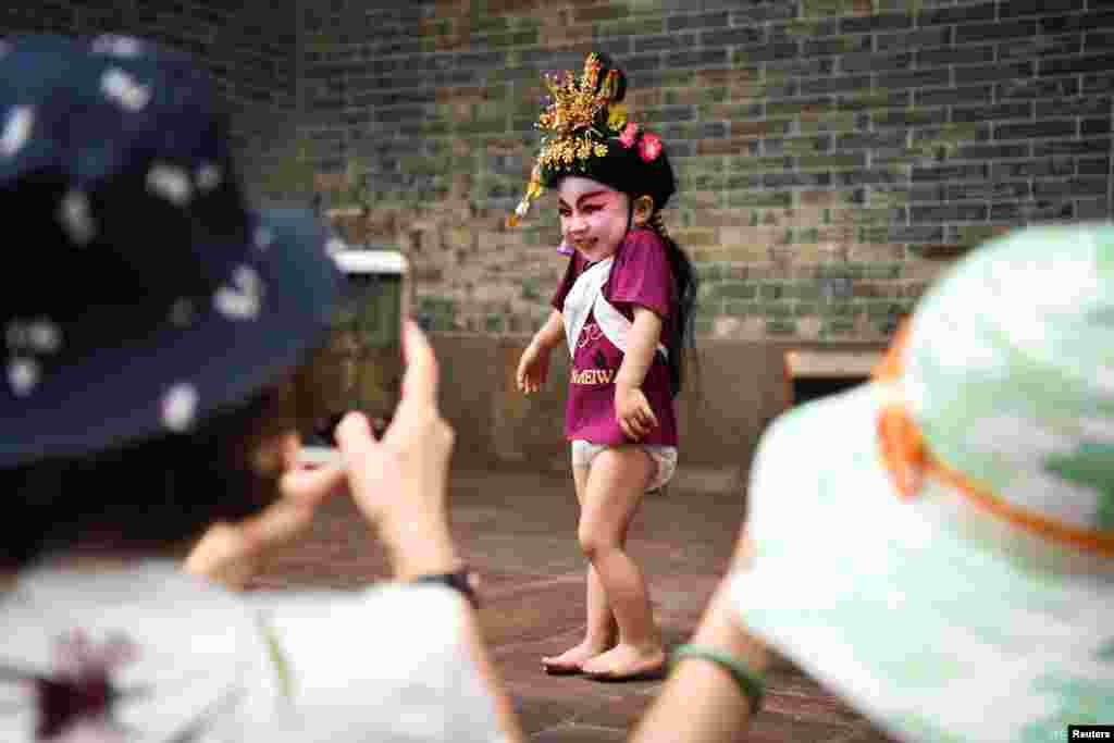អ្នកទស្សនាថតរូបក្មេងដែលស្លៀកពាក់សម្លៀកបំពាក់ប្រពៃណីមុនពេលសម្តែងនៅក្រុង Panyu ខេត្ត Guangdong ប្រទេសចិន។