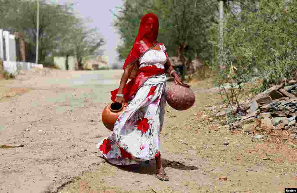 A woman carries earthen pots to fill them with drinking water on a hot summer day, on the outskirts of Ajmer, Rajasthan, India.