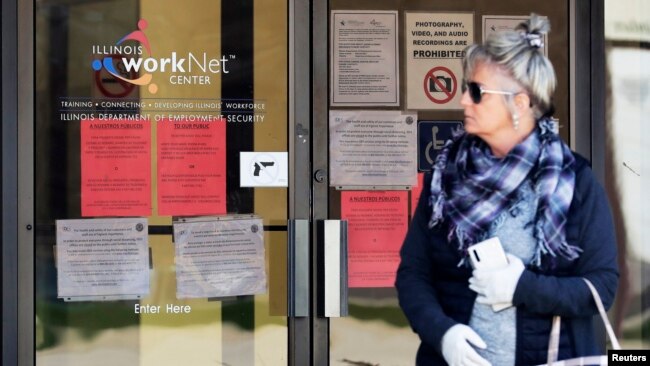 资料照片：一名失业妇女在伊利诺伊州政府就业安全局门前查看就业申请信息（2020年4月9日）