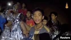 Boys from the under-16 soccer team trapped inside Tham Luang cave covered in hypothermia blankets react to the camera in Chiang Rai, Thailand, in this still image taken from a July 3, 2018 video by Thai Navy Seal. 