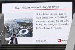 Seorang pria mengenakan masker, berjalan melewati layar yang menunjukkan berita tentang peringatan AS terhadap kunjungan ke Jepang di Tokyo, Selasa, 25 Mei 2021.
