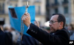 FILE - A protester holds up a crucifix as protestors gather in front of the city hall during a demonstration organized by a platform in defense of religious freedom, to condemn what they call "attacks on the rights of believers" in Barcelona, Spain.