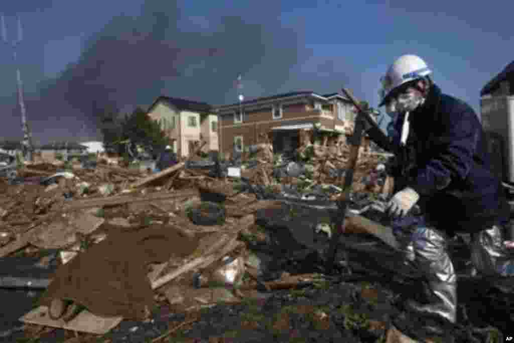 A body, covered in a blanket, lies in the rubble of a destroyed neighborhood as firefighters search the area in Sendai, Miyagi Prefecture, northeastern Japan, two days after a giant quake and tsunami struck the country's northeastern coast, March 13, 2011