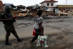 FILE - A woman walks past a Cameroonian elite Rapid Intervention Battalion (BIR) member in the city of Buea in the anglophone southwest region, Cameroon, Oct. 4, 2018.