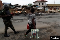 FILE - A woman walks past a Cameroonian elite Rapid Intervention Battalion (BIR) member in the city of Buea in the anglophone southwest region, Cameroon, Oct. 4, 2018.