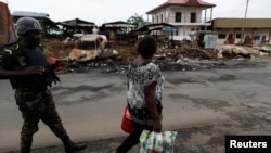 FILE - A woman walks past a Cameroonian elite Rapid Intervention Battalion (BIR) member in the city of Buea in the anglophone southwest region, Cameroon, Oct. 4, 2018.