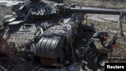 A pro-Russian rebel crouches in front of a destroyed Ukranian army tank in the village of Spartak, on the outskirts of Donetsk, March 16, 2015. 