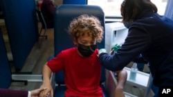 FILE - Max Cuevas, 12, holds his mother's hand as he receives the Pfizer COVID-19 vaccine from nurse practitioner Nicole Noche at Families Together of Orange County in Tustin, California, May 13, 2021.