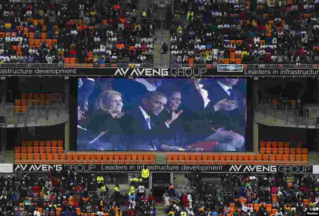 U.S. President Barack Obama (C) and his wife Michelle are seen on a big screen at the First National Bank (FNB) Stadium, also known as Soccer City, during the national memorial service for former South African President Nelson Mandela in Johannesburg Dece