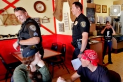 Guests watch as police officers leave the Horseshoe Cafe as owner Debbie Thompson, right, cries in the kitchen in Wickenburg, Ariz., May 1, 2020. The officers told Thompson she had to shut down guest seating to comply with state stay-at-home rules.