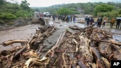 FILE —Passengers from stranded vehicles stand next to the debris from floodwaters, on the road from Kapenguria, in West Pokot county, in western Kenya Saturday, Nov. 23, 2019. 