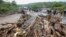 FILE —Passengers from stranded vehicles stand next to the debris from floodwaters, on the road from Kapenguria, in West Pokot county, in western Kenya Saturday, Nov. 23, 2019. 