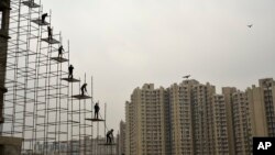 Para pekerja India berdiri di atas batang baja yang ditancapkan di atas tanah ke atas gedung yang sedang dibangun di Greater Noida, India, 12 Februari 2018. (Foto: dok).