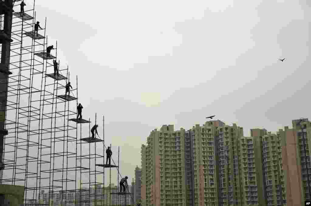 Indian laborers work on a scaffolding at a building construction site in Greater Noida.