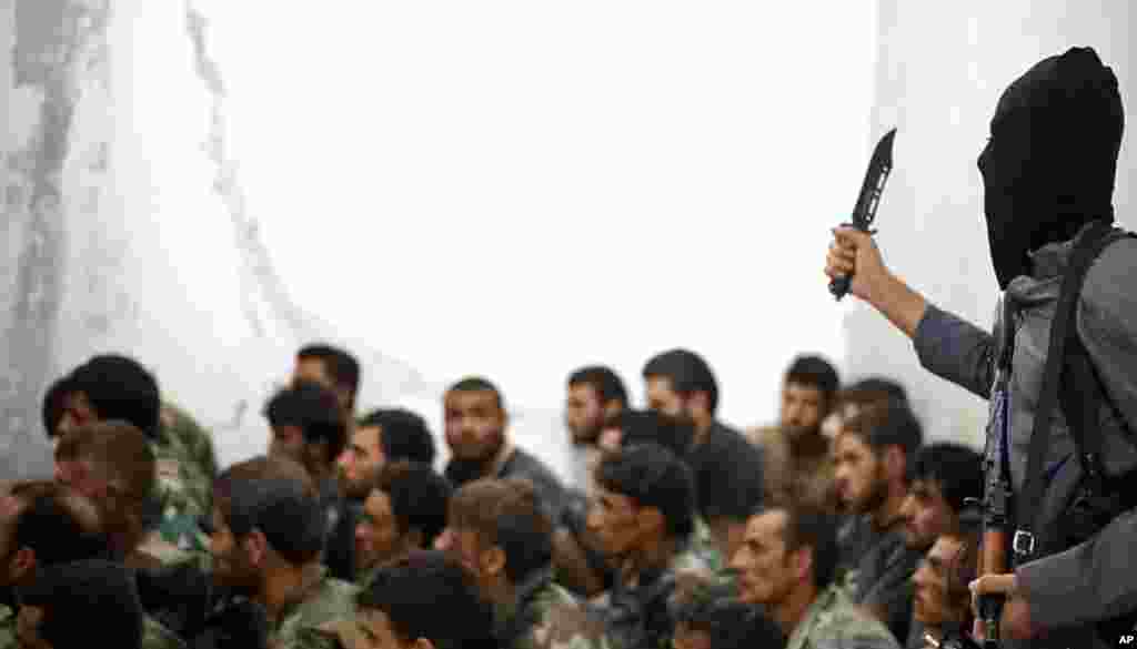 This undated image posted on Wednesday, Aug. 27, 2014 by the Raqqa Media Center, a Syrian opposition group, shows a fighter from the Islamic State armed with a knife and an automatic weapon next to captured Syrian army soldiers and officers, following the battle for the Tabqa air base, Raqqa, Syria. &nbsp;
