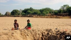 FILE - In this Nov. 11, 2020, photo, children sit by a water hole in a dry river bed in the remote village of Fenoaivo, Madagascar. 