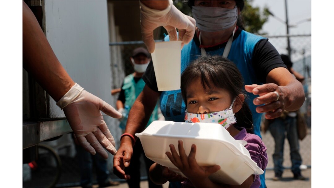 A child gets a meal from the mobile dining rooms program as people who have not been able to work because of the COVID-19 pandemic line up for a meal outside the Iztapalapa hospital in Mexico City, Wednesday, May 20, 2020.