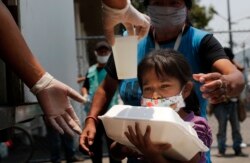A child gets a meal from the mobile dining rooms program as people who have not been able to work because of the COVID-19 pandemic line up for a meal outside the Iztapalapa hospital in Mexico City, Wednesday, May 20, 2020.