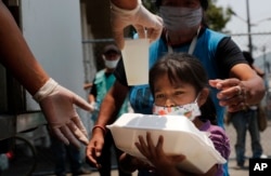A child gets a meal from the mobile dining rooms program as people who have not been able to work because of the COVID-19 pandemic line up for a meal outside the Iztapalapa hospital in Mexico City, Wednesday, May 20, 2020.