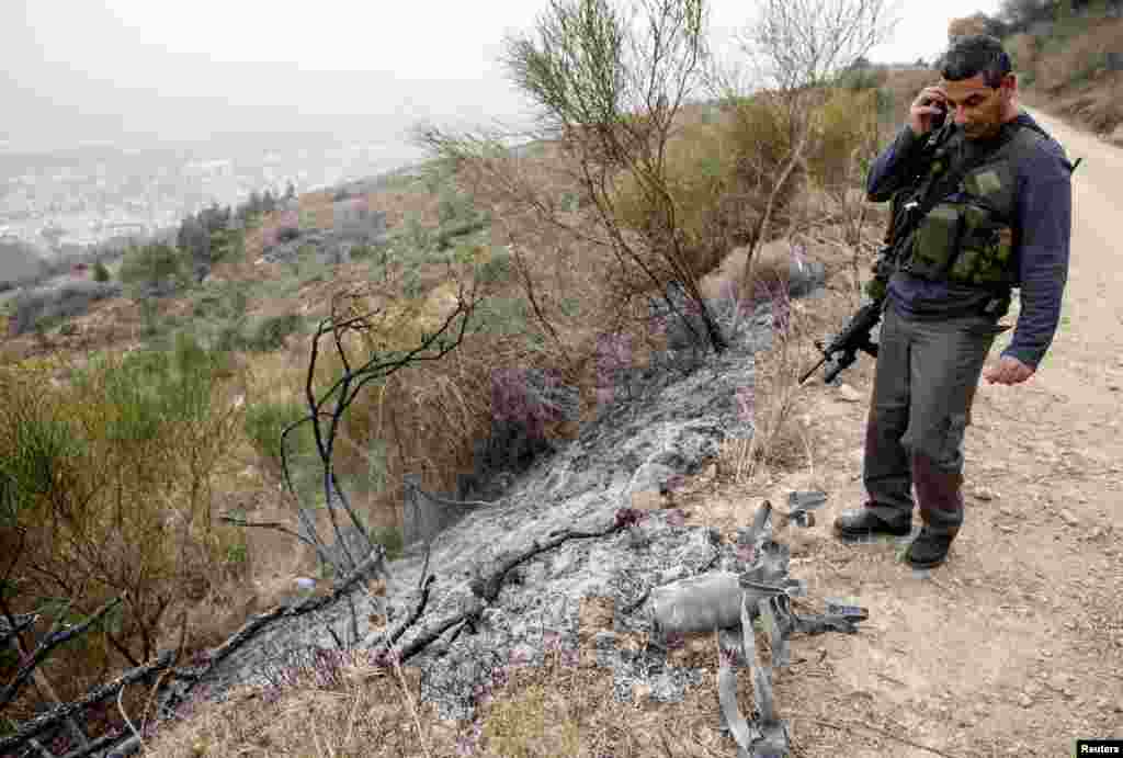 An Israeli security coordinator stands next to the remains of a rocket after it landed near the northern town of Kiryat Shmona, Israel, Dec. 29, 2013.