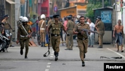 Sri Lankan police clear the area while Special Task Force Bomb Squad officers inspect the site of an exploded van near a church that was attacked yesterday in Colombo, April 22, 2019.