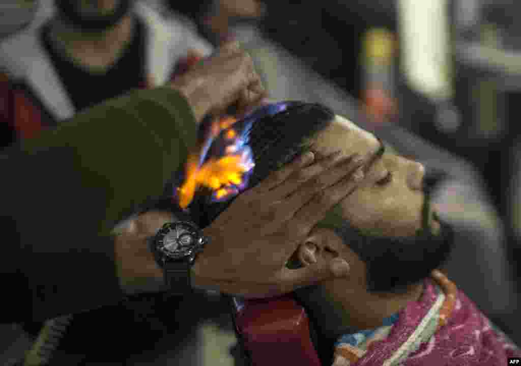 Barber Ramadan Edwan performs a technique that utilizes fire to straighten his client&#39;s hair, in the Rafah refugee camp, in the southern Gaza Strip.