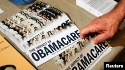 FILE - A Tea Party member reaches for a pamphlet titled "The Impact of Obamacare," at a "Food for Free Minds Tea Party Rally" in Littleton, New Hampshire, Oct. 27, 2012. 