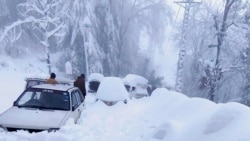 In this photo provided by the Inter Services Public Relations, people walk past vehicles trapped in a heavy snowfall-hit area in Murree, Pakistan, Jan. 8, 2022.