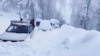 In this photo provided by the Inter Services Public Relations, people walk past vehicles trapped in a heavy snowfall-hit area in Murree, Pakistan, Jan. 8, 2022. 