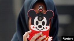FILE - A girl uses her mobile phone in Jakarta, Indonesia, July 5, 2017. A researcher in Britain says her findings suggest young girls who are more active on social media have lower levels of well-being in their teens.