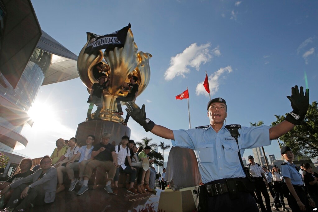 在香港湾仔金紫荆广场( Golden Bauhinia Square),警察阻止抗议者爬上金紫荆雕塑。雕塑上已经有不少人,雕塑顶部挂着黑布,写着标语“无条件释放刘晓波”和“香港市民要真普选”(2017年6月28日)。这座大型雕塑是1997年香港回归中国时北京送的礼物。