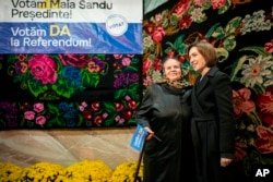 Moldova's President Maia Sandu, right, is pictured with a woman holding a flag reading "We Vote Yes to the Referendum" during an electoral meeting in Magdacesti, Moldova, Oct. 17, 2024.