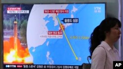 Seorang perempuan melewati layar TV di stasiun Kereta Seoul, yang sedang menyiarkan berita Korea Utara mengancam menyerang Guam dengan misil. 10 Agustus 2017. 