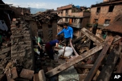 FILE - In this April 27, 2015 file photo a Nepalese family collects belongings from their home destroyed in an earthquake, in Bhaktapur on the outskirts of Kathmandu, Nepal.