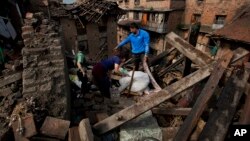 FILE - In this April 27, 2015 file photo a Nepalese family collects belongings from their home destroyed in Saturday's earthquake, in Bhaktapur on the outskirts of Kathmandu, Nepal. Last year saw the lowest financial costs from natural disasters worldwide since 2009 as the El Nino weather phenomenon reduced hurricane activity in the North Atlantic, a leading insurer said, Jan. 4, 2016.
