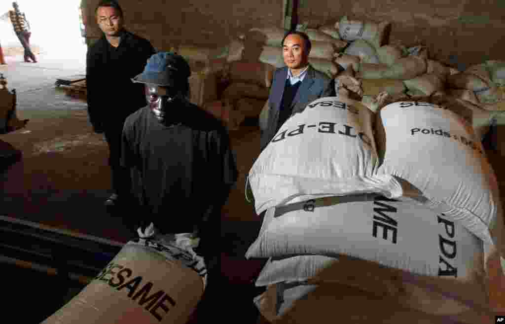 在塞内加尔首都达卡的一家芝麻厂，一名当地工人在堆放一袋袋的种子，中国投资商欧阳日坪（右）在一旁观看（2009年2月）。