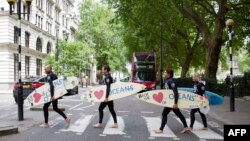 FILE - Climate change campaigners in wetsuits and holding surfboards cross the road by the Houses of Parliament, London, June 17, 2015.