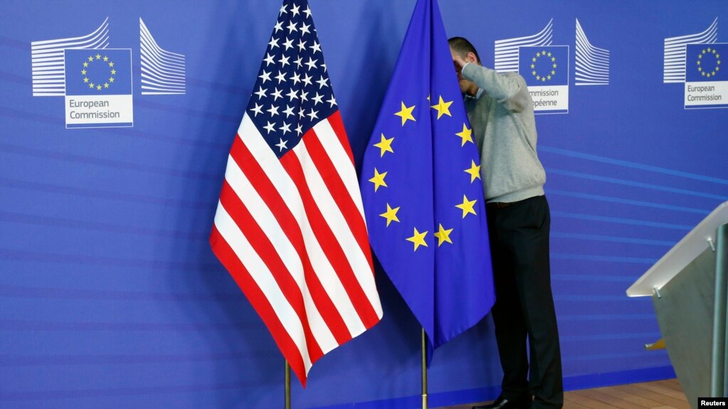 资料照片：一名工作人员在欧盟与美国贸易谈判的会场调整欧盟和美国的旗帜。（2013年11月11号)(photo:VOA)